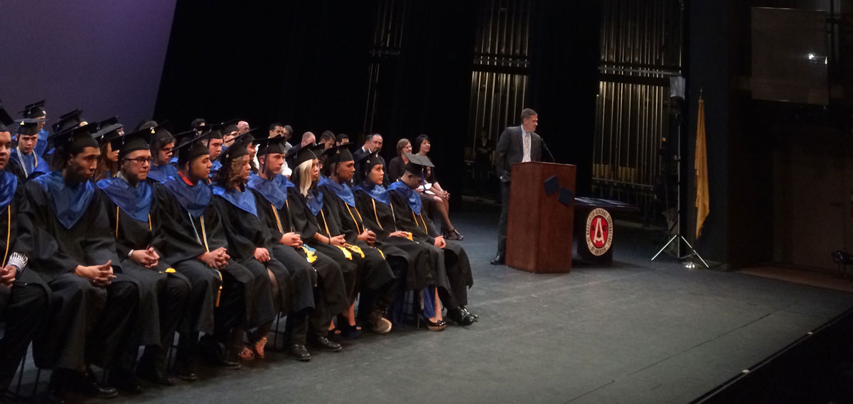 Students on stage for graduation in cap & gowns.