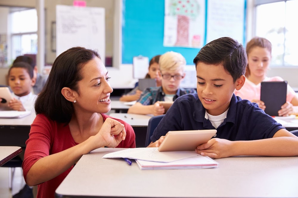 Female teacher kneeling next to male student sitting at desk