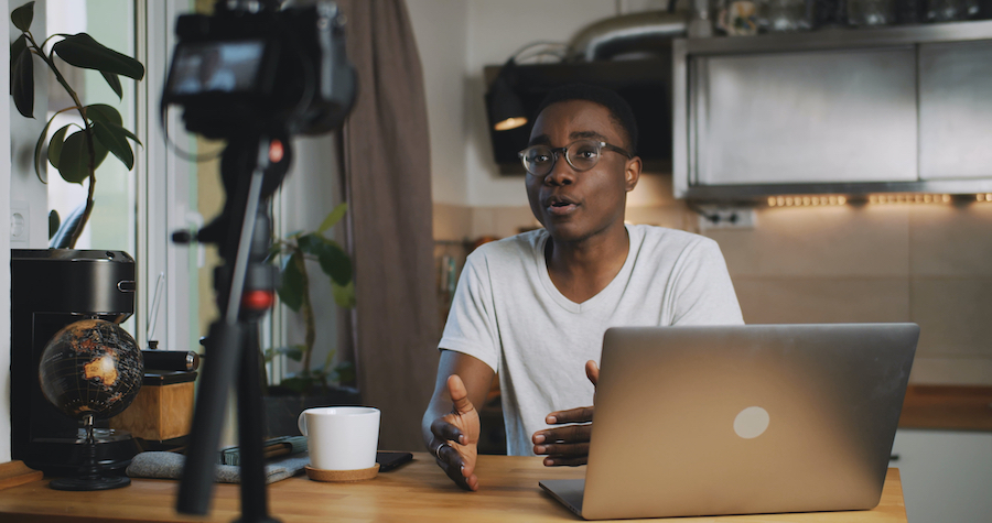 Male student filming a video with camera equipment and computer in front of him