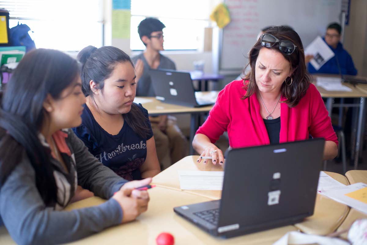 teacher sitting with two students working on assignment