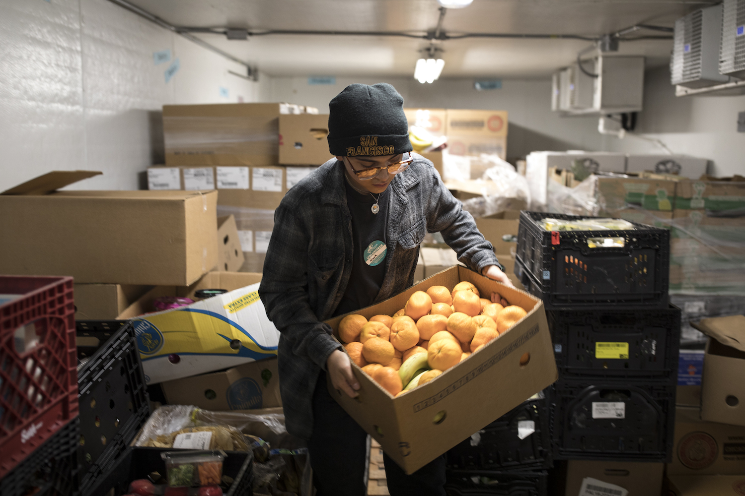 Person wearing hat lifting box of produce in storage room