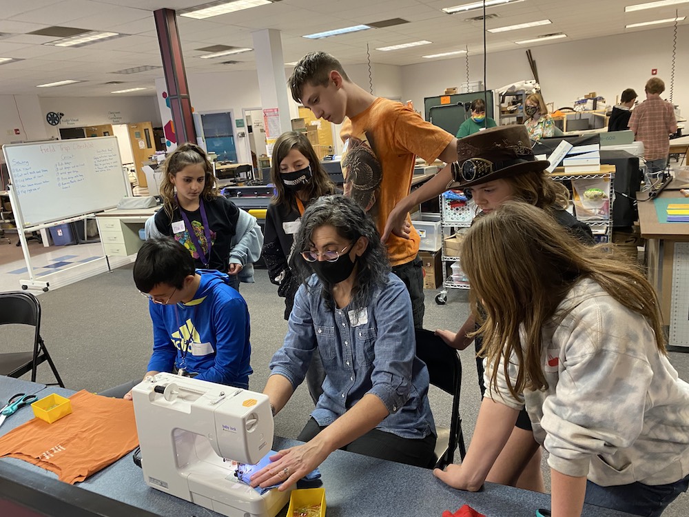 Teacher using sewing machine with students around observing