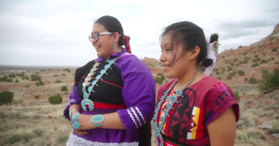 Two Zuni pueblo students in traditional clothing standing in desert background