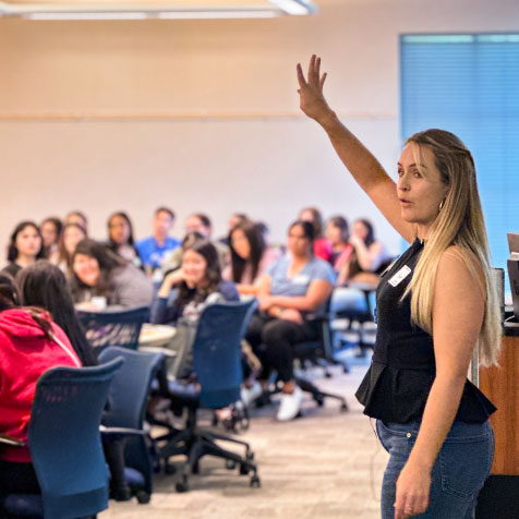 woman raises her hand at the front of a classroom