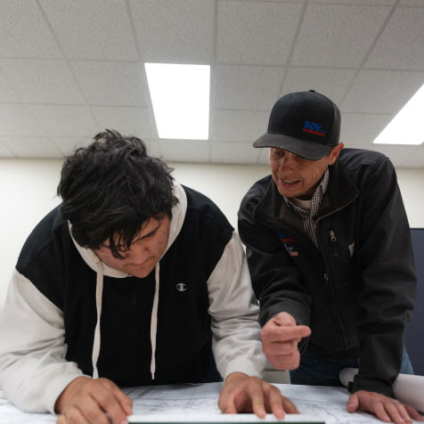 A student measures plans while his mentor looks on.