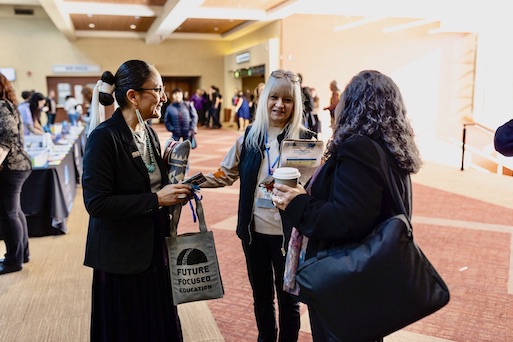 Three women speaking to each other in the lobby of a conference.